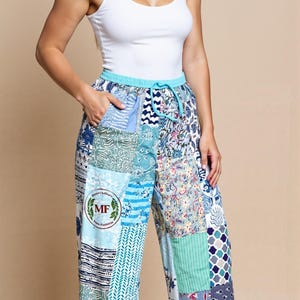 Peut inclure: Pantalon à imprimé patchwork avec taille élastique. Le pantalon présente une variété de motifs bleus et blancs, notamment des motifs floraux, géométriques et rayés. Un débardeur blanc est porté avec le pantalon. Le pantalon a un écusson avec un logo.