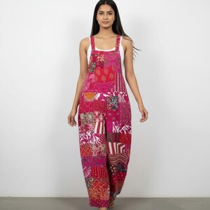 May include: A patchwork jumpsuit in shades of pink, red, and white. The jumpsuit features a variety of patterned fabric patches, with wide legs and adjustable straps. The model is wearing a white tank top underneath.