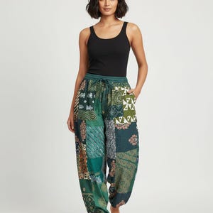 Peut inclure: Une personne portant un débardeur noir et un pantalon vert à patchwork. Le pantalon présente une variété de motifs dans les tons verts, bleus et marron. Le pantalon a une taille à cordon et des chevilles resserrées.
