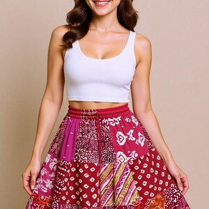 Può includere: Una donna indossa un top corto bianco e una gonna patchwork. La gonna presenta vari motivi nei toni del rosso, rosa e bianco. Ha un punto vita con coulisse e un design a balze. La gonna è lunga circa 45 cm.