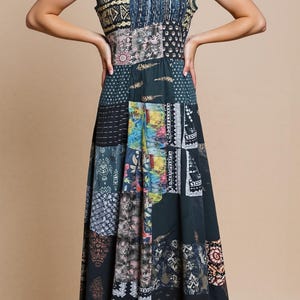 Könnte beinhalten: Ein ärmelloses Patchwork-Maxikleid in den Farbtönen Teal, Schwarz und Beige. Das Kleid hat einen Rundhalsausschnitt und einen fließenden Rock, der aus verschiedenen Stoffbahnen mit Mustern besteht. Das Model trägt schwarze High Heels.