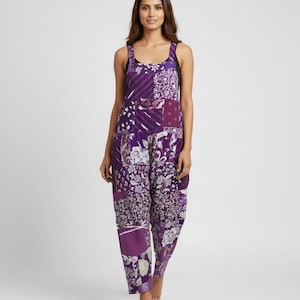 May include: A patchwork jumpsuit in shades of purple and white. The jumpsuit features a square neckline, wide straps, and a loose, comfortable fit. The fabric is patterned with floral and geometric designs.