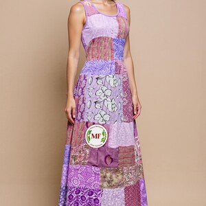 Op de afbeelding: Een mouwloze patchwork maxi-jurk in tinten paars, lavendel en roze. De jurk heeft een verscheidenheid aan bloemen- en geometrische patronen, met een getailleerd lijfje en een zwierige rok. De jurk wordt gedragen met zwarte hakken.