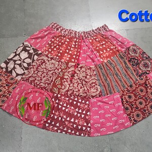 May include: A patchwork skirt in shades of pink, red, and brown, featuring various floral and geometric patterns. The word "Cotton" is displayed in blue. The skirt has an elastic waistband.