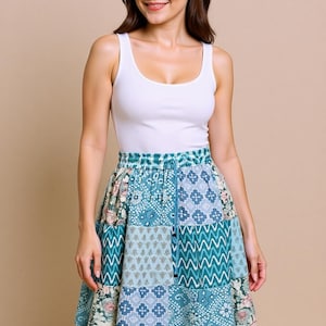 Può includere: Una donna indossa una canotta bianca e una gonna patchwork blu. La gonna presenta vari motivi geometrici e floreali nei toni del blu, verde e bianco. La gonna ha una vita con coulisse.