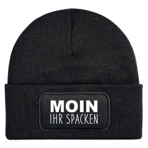 Könnte beinhalten: Schwarze Beanie-Mütze mit rechteckigem Aufnäher. Der Aufnäher zeigt den weißen Text "MOIN IHR SPACKEN". Die Mütze ist aus Rippstrick gefertigt. Ein lässiges und warmes Winteraccessoire.