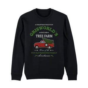 Könnte beinhalten: Schwarzes Sweatshirt mit einem festlichen Motiv. Es zeigt einen roten Lastwagen, der einen Weihnachtsbaum transportiert, mit dem grünen Schriftzug "Griswold's Tree Farm". Der Text enthält auch "A Christmas Tradition" und "Home of the Fun Old Fashioned Family Christmas".