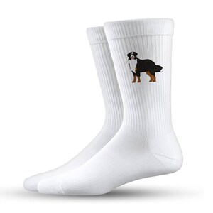 Könnte beinhalten: Ein Paar weiße Crew-Socken mit einer Illustration eines Berner Sennenhundes. Der Hund ist in Schwarz, Braun und Weiß dargestellt. Die Socken sind aus weichem, geripptem Material.