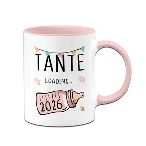Könnte beinhalten: Weißer Keramikbecher mit rosa Innenraum und Henkel. Der Becher zeigt das Wort "TANTE" in Schwarz, darunter "LOADING...". Eine Babyflaschen-Grafik mit "2026" ist ebenfalls auf dem Becher abgebildet, zusammen mit einem Banner und Babyfüßen.