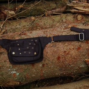 May include: A black canvas fanny pack with a flap closure and multiple metal eyelets. The pack has a long adjustable strap and is shown on a wooden background.