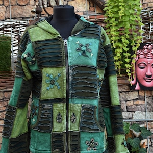 Könnte beinhalten: Eine grüne Kapuzenjacke mit Reißverschluss im Patchwork-Design, bestehend aus abwechselnden einfarbigen Stoffbahnen und Details mit horizontalen Schlitzen. Das Kleidungsstück ist mit gestickten Blumenmotiven und kleinen Perlen verziert.