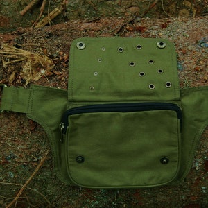 May include: A green canvas fanny pack with a zippered pocket and multiple eyelets. The pack has a wide belt with a buckle.