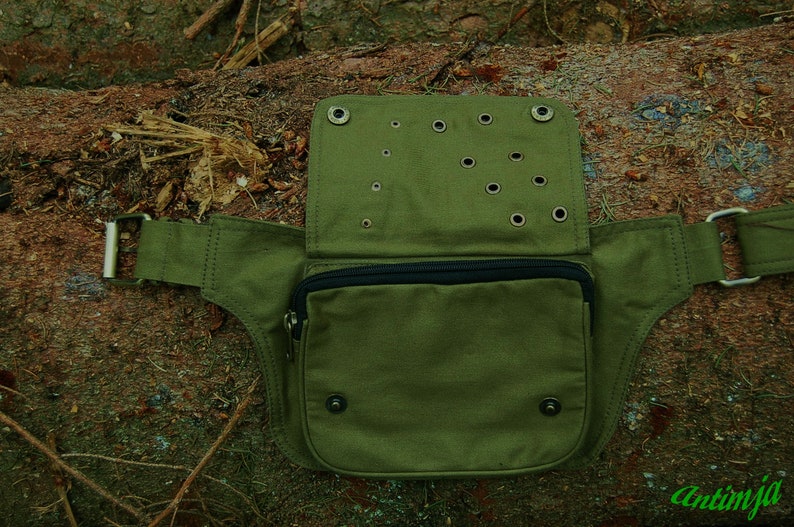 May include: A green canvas fanny pack with a zippered pocket and multiple eyelets. The pack has a wide belt with a buckle.
