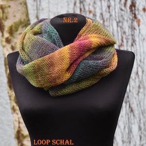 Könnte beinhalten: Ein gestrickter Loop-Schal mit einem bunten Farbverlauf in Gelb, Pink, Grün und Violett. Der Schal wird auf einer schwarzen Schaufensterpuppe präsentiert. Der Text NR.2 ist oben und der Text LOOP SCHAL ist unten zu sehen.