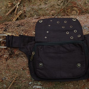 May include: A black canvas fanny pack with a zippered pocket and multiple grommets. The pack has a buckle closure and a strap.