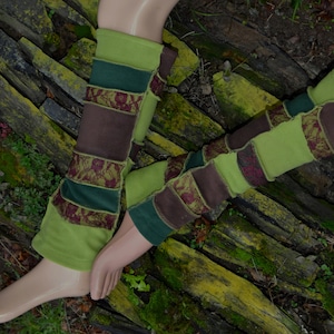 Könnte beinhalten: Ein Paar Stulpen mit einem Patchwork-Design aus lindgrünen, dunkelgrünen und braunen Stoffbahnen sowie Abschnitten aus dunkelroter Spitzenstickerei. Der Text ANTIMJA ist vertikal in Grün auf der linken Seite des Bildes aufgedruckt.