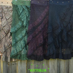 Könnte beinhalten: Vier mehrschichtige Spitzröcke in den Farben Braun, Grün, Lila und Schwarz hängen an einem Holzzaun. Jeder Rock hat ein Rüschendesign und einen kontrastierenden Bund. Die Röcke sind im Bohemian-Stil gehalten.