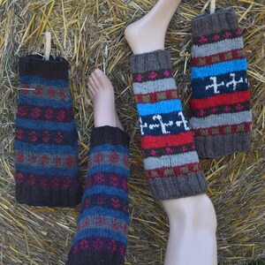 Könnte beinhalten: Gestrickte Beinwärmer in Braun-, Blau-, Rot- und Grautönen mit geometrischen Mustern. Ein Paar wird an einem Schaufensterbein präsentiert, während ein anderes Paar an einer Wäscheklammer hängt. Die Beinwärmer sind aus dickem, strukturiertem Garn gefertigt.
