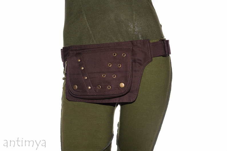 May include: A brown canvas fanny pack with a flap closure and metal accents. The fanny pack is worn around the waist and has a strap that can be adjusted.