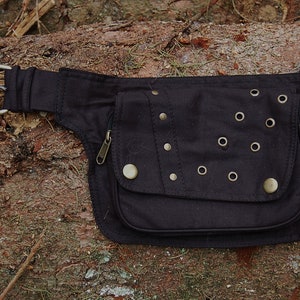 May include: Black canvas fanny pack with a zippered pocket and multiple metal eyelets and studs.