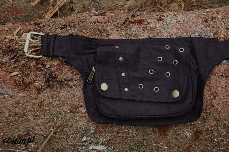 May include: Black canvas fanny pack with a zippered pocket and multiple metal eyelets and studs.