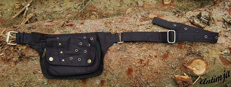 May include: A black canvas belt bag with a large pocket and multiple metal eyelets. The bag has a long adjustable strap with a silver buckle.