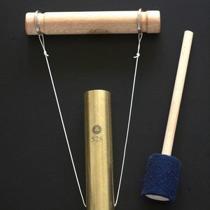 Puede incluir: Un tubo de metal dorado con un mazo de madera y una barra de madera con dos anillos unidos a él. El tubo tiene el número 528 impreso en él.