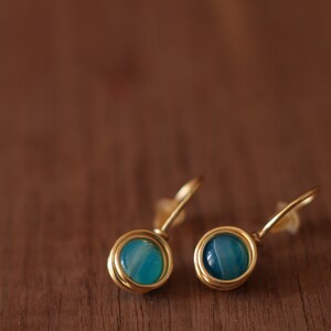 May include: A pair of gold earrings with blue agate stones. The earrings are made with wire wrapped around the stones.