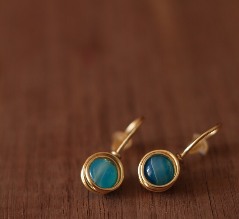 May include: A pair of gold earrings with blue agate stones. The earrings are made with wire wrapped around the stones.