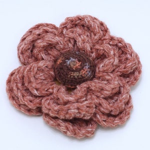 May include: A crocheted flower with a brown center, made with a combination of pink and white yarn.