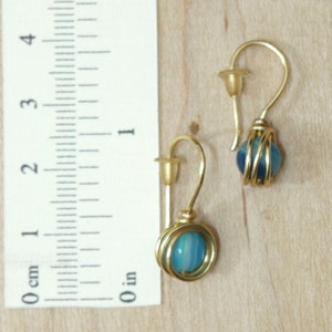 May include: A pair of gold earrings with blue agate stones wrapped in gold wire. The earrings are about 1 inch long.