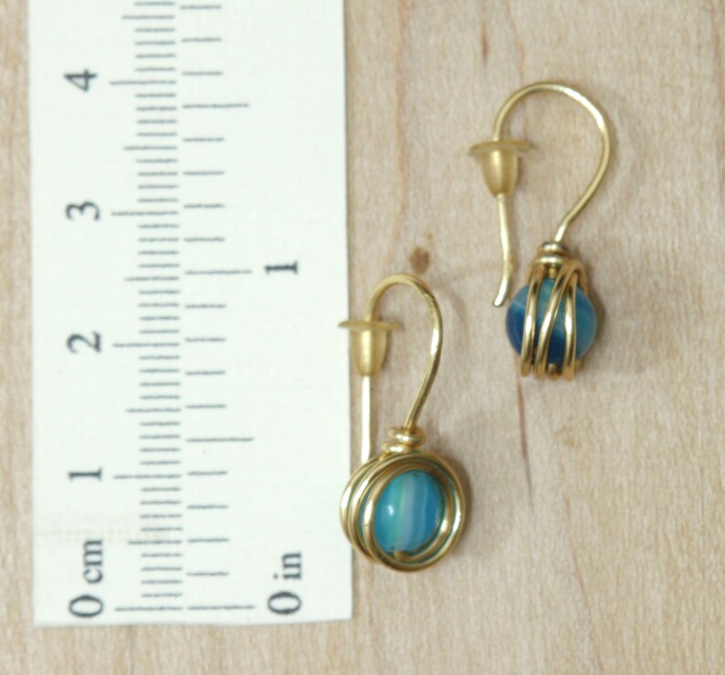 May include: A pair of gold earrings with blue agate stones wrapped in gold wire. The earrings are about 1 inch long.