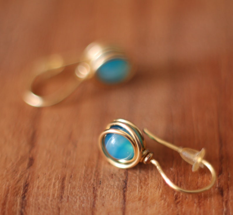May include: A pair of gold wire earrings with blue gemstone accents. The earrings are made with a simple wire design and feature a round blue gemstone in the center.