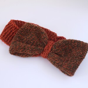 Puede incluir: Una diadema de punto marrón y verde con un gran lazo. La diadema está hecha de un hilo suave y texturizado.