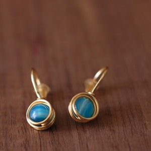 May include: A pair of gold earrings with blue agate stones. The earrings are made with wire wrapped around the stones.