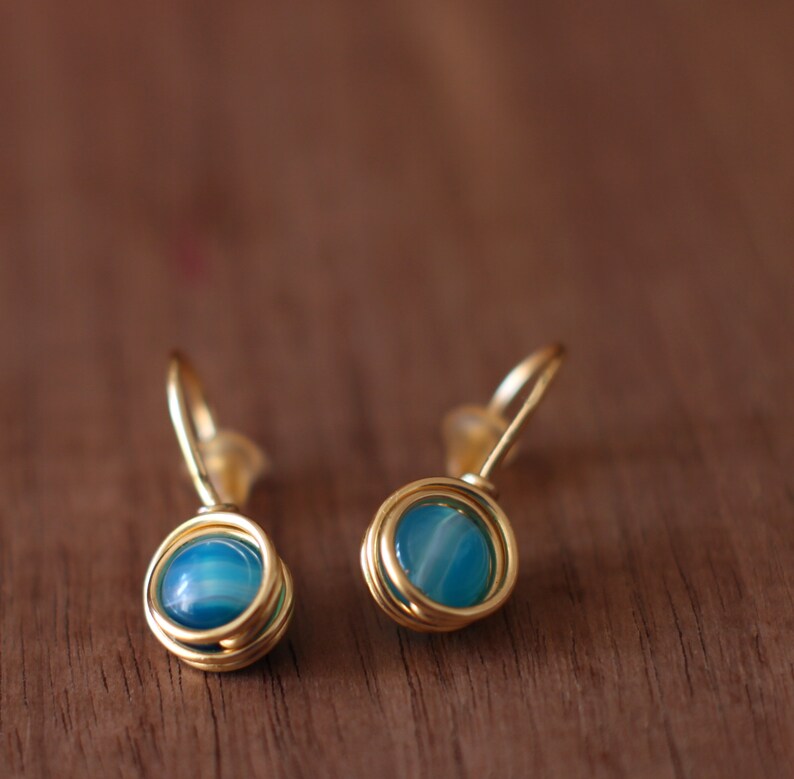 May include: A pair of gold earrings with blue agate stones. The earrings are made with wire wrapped around the stones.
