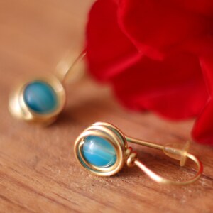 May include: A pair of gold earrings with blue agate stones. The earrings are made of wire that is wrapped around the stones.