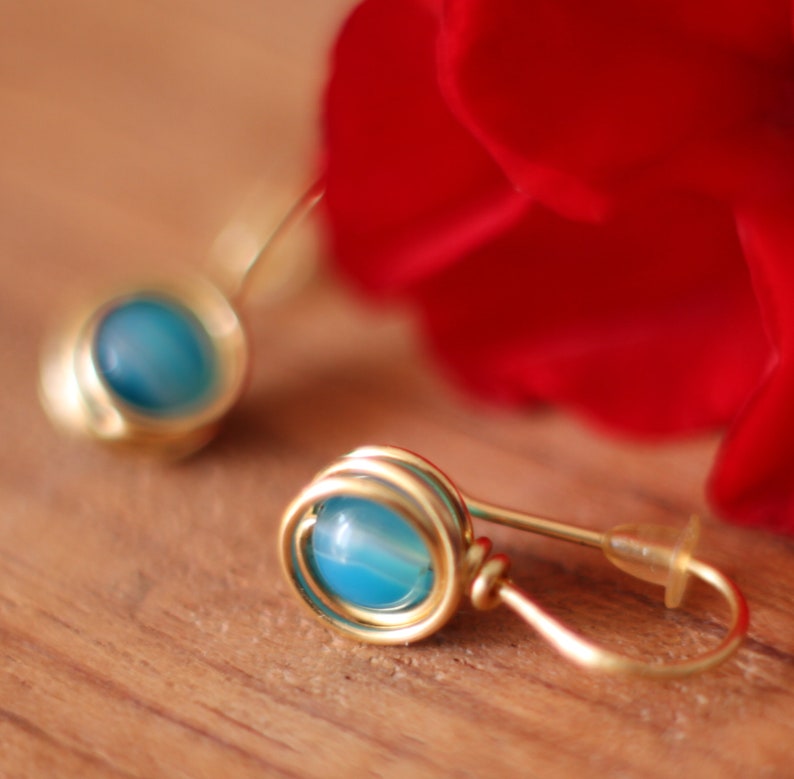 May include: A pair of gold earrings with blue agate stones. The earrings are made of wire that is wrapped around the stones.