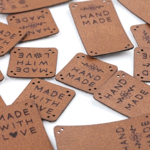 Könnte beinhalten: Eine Sammlung brauner Leder-Etiketten mit verschiedenen Sätzen, darunter "Hand Made", "Made with Love" und "Made with Love".