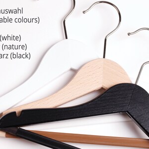 May include: Three wooden hangers in white, natural wood, and black. The text "Farbauswahl (available colours)" is written above the hangers. Below the text are the words "wei&szlig; (white)", "natur (nature)", and "schwarz (black)".