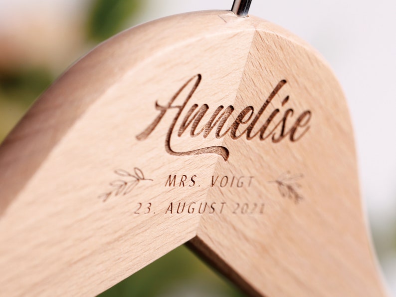 May include: A wooden hanger with the name "Annelise" engraved on it, along with the text "MRS. VOIGT" and "23. AUGUST 2021".