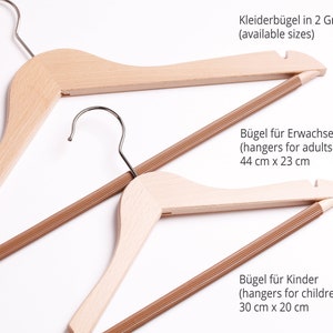 May include: Two wooden hangers, one larger and one smaller, with brown fabric covered bars. The larger hanger measures 44 inches by 23 inches and the smaller hanger measures 30 inches by 20 inches. The text "Kleiderb&uuml;gel in 2 Gr&ouml;&szlig;en (available sizes)" is at the top of the image. The text "B&uuml;gel f&uuml;r Erwachsene (hangers for adults) 44 cm x 23 cm" is in the middle of the image. The text "B&uuml;gel f&uuml;r Kinder (hangers for children) 30 cm x 20 cm" is at the bottom of the image.