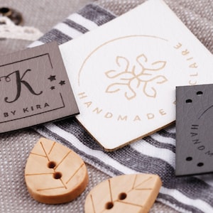 Op de afbeelding: Drie verschillende lederen labels met een bloemmotief en de tekst "Handmade" op twee van de labels. Het derde label heeft de tekst "K by Kira" en drie sterren.