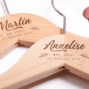 May include: Two wooden hangers with the names "Martin" and "Annelise" engraved on them. The hangers are personalized with the text "Mr. Voigt" and "Mrs. Voigt" and the date "23 August 2021".