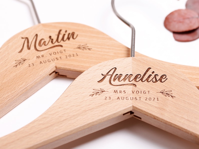 May include: Two wooden hangers with the names "Martin" and "Annelise" engraved on them. The hangers are personalized with the text "Mr. Voigt" and "Mrs. Voigt" and the date "23 August 2021".
