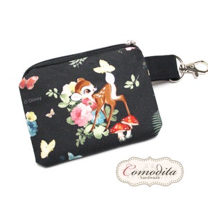 Könnte beinhalten: Schwarze Reißverschlusstasche mit einem Blumendruck, der einen Bambi-Cartoon, Pilze und Schmetterlinge zeigt. Die Tasche hat einen schwarzen Riemen mit einem silbernen Schlüsselring. Der Text "© Disney" ist auf der Tasche aufgedruckt.