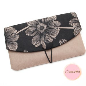 Könnte beinhalten: Eine beige Clutch mit einem schwarzen Klappverschluss, der mit einem beigen Blumenmuster verziert ist. Die Clutch hat ein schlichtes Design mit einem schwarzen Kordelverschluss. Die Gesamtästhetik ist elegant und für verschiedene Anlässe geeignet.