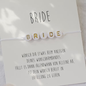 Puede incluir: Pulsera blanca con letras doradas que deletrean "BRIDE" en una tarjeta blanca con el texto "WÜNSCH DIR ETWAS BEIM ANLEGEN DEINES WUNSCHARMBANDES. FÄLLT ES DANN IRGENDWANN VON ALLEINE AB, IST DEIN WUNSCH BEREIT IN ERFÜLLUNG ZU GEHEN."