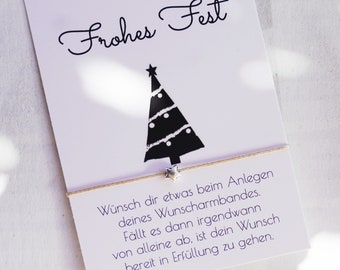 May include: A white card with the words "Frohes Fest" and a black Christmas tree illustration. A silver star charm bracelet is attached to the card. The card has German text.