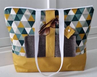 May include: A large yellow and green geometric patterned tote bag with white polka dots on the bottom. The bag has white straps and a small pocket with a white button.